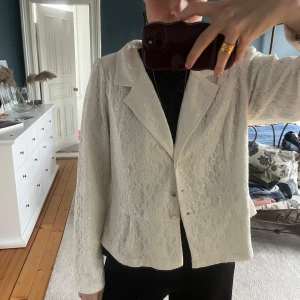 Vit spetskavaj från ZAY - Säljer en vit kavaj från ZAY med spetsdetaljer och klassisk krage. Kavajen har lång ärm, knäppning framtill. Perfekt för dig som vill ha en elegant och stilren look.