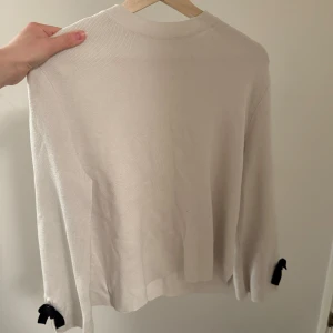Vit stickad tröja från Zara - Säljer en vit stickad tröja från Zara med svarta rosetter längst ner på ärmarna. Tröjan har lång ärm och är en del av deras winter collection💗