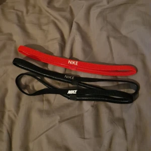 Nike hårband i rött och svart - Två svarta och ett rött hårband från Nike. Alla har Nike-loggan broderad framtill och är smala i modellen. Perfekta för att hålla håret på plats under träning eller vardag. Nästintill oanvända och I bra skick. Säljer pga att jag inte behöver använda de längre 😊