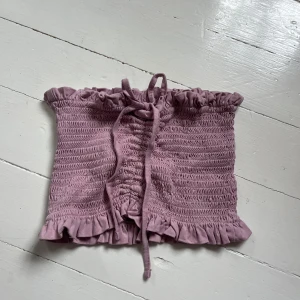 Ljuslila croppad tubtopp med volang och snörning - Superfin ljuslila tubtopp med smock, volangkant upptill och nertill samt knytning framtill. Perfekt för sommardagar och festivaler. Söt och trendig modell som passar till både jeans och kjol. Vid köp av flera blir det ett bättre pris. Skriv för fler bilder💞