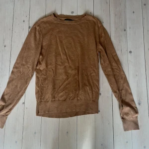 Beige stickad tröja - Säljer en enkel och stilren beige stickad tröja med rund halsringning. Tröjan har långa ärmar och ribbade muddar vid ärmslut och nederkant. Perfekt för lager-på-lager under kyligare dagar.