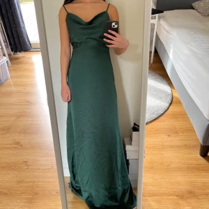 Mörkgrön långklänning med smala axelband - Säljer en elegant mörkgrön långklänning med smala justerbara axelband och lätt draperad urringning. Klänningen har en figurnära passform upptill och faller snyggt längs kroppen. Kjolen har extra tyg, så det faller fint. Perfekt för bal eller festliga tillfällen. Dragkedja där bak. Klänningen är 141 cm lång från axeln och jag är 171 cm 🤍