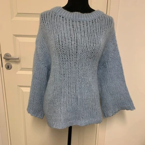 Ljusblå stickad tröja från Fransa - Mysig ljusblå stickad tröja från Fransa med grovstickat mönster och rund halsringning. Tröjan har långa, lite vidare ärmar och en avslappnad passform. Perfekt för kyliga dagar och enkel att styla till olika outfits.
