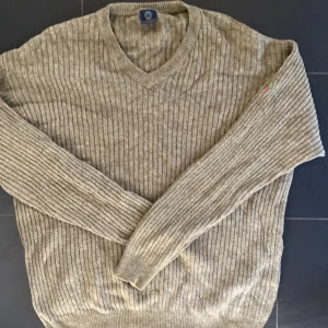 Beige ribbstickad tröja från Boomerang - Säljer en beige ribbstickad tröja från Boomerang med v-ringad hals. Tröjan har långa ärmar och en diskret broderad detalj på ena ärmen. Perfekt för lager-på-lager under kyliga dagar. Stor passform