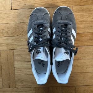 Grå Adidas Gazelle sneakers - Säljer ett par klassiska Adidas Gazelle sneakers i grå mocka, storlek 40. De är endast använda ett fåtal gånger och är i mycket bra skick! Säljer då de tyvärr inte passar mig.