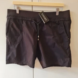 Shorts med dragsko från Esmara strl 44 - Svarta shorts från Esmara med elastisk midja och dragsko. Två fickor fram och två falska fickor bak med lock. Tillverkade i ett lätt och bekvämt material. Storlek 44. Kan hämtas i Vallentuna.