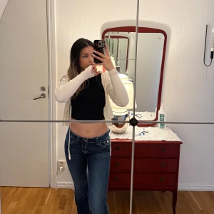 Mörkblå bootcut jeans med vita sömmar - Säljer ett par mörkblå bootcut jeans med vita kontrastsömmar och klassiska fickor bak med lock och knapp. Jeansen har låg midja och en snygg passform som sitter tajt upptill och släpper vid benen. Perfekta för en avslappnad och trendig look. Är i helt nytt skick. Storleken är 158/164. Har resår band på insidan så går att justera storleken på midjan.