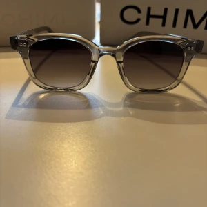 Chimi 02 Grey - Snygga solglasögon från CHIMI i transparent grå plast med rundade rektangulära bågar och mörktonade glas. Perfekt accessoar för att lyfta din stil med en modern touch.