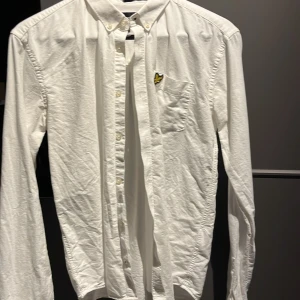 Vit skjorta från Lyle & Scott Junior - Klassisk vit skjorta från Lyle & Scott Junior i storlek 15/16 yr( runt 164 cm) med knappkrage och bröstficka med broderad logga. Skjortan är tillverkad i 100% bomull och har långa ärmar. Perfekt för en clean och stilren look.        