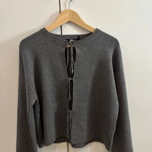 Grå stickad tröja med knyt från Gina Tricot - Säljer en grå stickad tröja från Gina Tricot med tre knyt framtill. Storlek XS men passar som en liten S också. (Mått går att lösa)