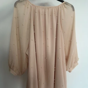 Beige blus med pärldetaljer - Säljer en superfin beige blus med transparenta, trekvartsärmade ärmar och små pärlor över hela tyget. Blusen har en lös passform och faller snyggt. Perfekt för dig som gillar romantiska detaljer och en luftig känsla.