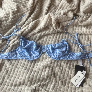 Blommig bikiniöverdel från NA-KD - Super söt bikiniöverdel från NA-KD i storlek 75C💗 Oanvänd med lappar kvar💕 Den har ett gulligt mönster med blommor och band att knyta vid axlarna🩷