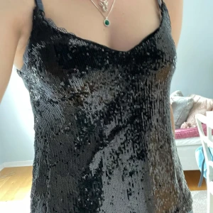 Svart paljettlinne med tunna axelband - Står att den är såld men är inte det. Säljer ett svart linne täckt av glittriga paljetter. Linnet har tunna axelband och en v-ringad halsringning. Perfekt för att sticka ut på festen!🩷