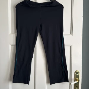 Svarta träningsbyxor från Röhnisch med blå detaljer - Svarta träningsbyxor från Röhnisch med smala blå linjer längs sidorna. Byxorna har en normal passform och är tillverkade i ett stretchigt syntetmaterial som passar perfekt för träning.