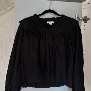 Svart volang blus Gina Tricot young - Svart blus med volanger från gina tricot young i storlek 158-164. Passar någon som har XS kanske S i vanliga fall eller barnstorlekar.  Lite urtvättad svart och har ett hål i vänster armhålla. Se bild 4 och 5. Obs bild 4 är hålet utsträckt och på 5 är hålet som de ser ut som vanligt. Köparen står för frakt. Priset går att diskutera, vill bli av med den för har för många liknande och är lite för liten för mig. Så bara hör av er!! KAN ABSOLUT GÅ NER I PRIS VID SNABB AFFÄR ELLER BUNDLE!