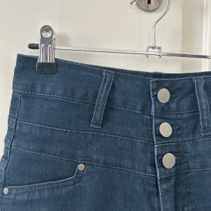 Mörkblå högmidjade jeansshorts med knappar - Snygga mörkblå jeansshorts med hög midja och tre silvriga knappar framtill. Perfekta för sommaren och lätta att matcha med olika toppar. Aldrig använda, nyskick! 