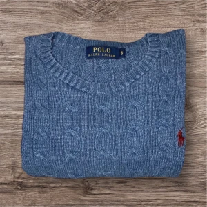 Blå stickad tröja från Polo Ralph Lauren - Säljer en klassisk blå stickad tröja från Polo Ralph Lauren med kabelstickat mönster och rund hals. Tröjan har långa ärmar och en liten röd broderad logga på bröstet. Perfekt för en stilren och tidlös look.