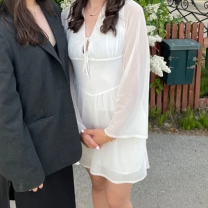 Vit klänning  - Säljer en söt vit kortklänning med långa, transparenta ärmar och v-ringning med knyt framtill. Perfekt till student eller andra evenemang! 