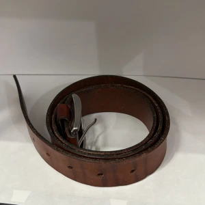 Brunt skärp från H&M i skinn - Säljer ett brunt bälte från H&M, tillverkat i Italien. Bältet är gjort av skinn och har ett klassiskt silverfärgat spänne. Passar perfekt till jeans eller chinos och har flera justerbara hål.