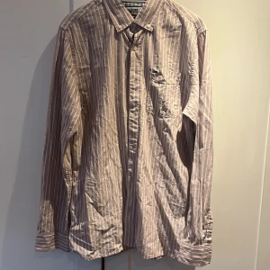 Rosa och vit randig skjorta från Hilfiger Denim - Säljer en snygg rosa och vit randig skjorta från Hilfiger Denim. Skjortan har klassisk krage, bröstficka med liten logga och långa ärmar. Perfekt för dig som gillar en stilren och avslappnad look.