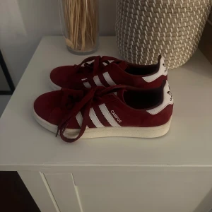Adidas Campus Collegiate Burgundy/White - Säljer ett par Adidas Campus sneakers i vinröd mocka med vita ränder och vit sula. Klassisk modell med snörning och låg profil, perfekt för en stilren vardagslook. 
