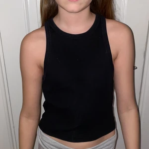 Svart ribbad linnetopp - Säljer en svart ribbad linnetopp med sportig skärning och rund halsringning. Toppen är ärmlös och har en tight passform, perfekt för en enkel och stilren look.