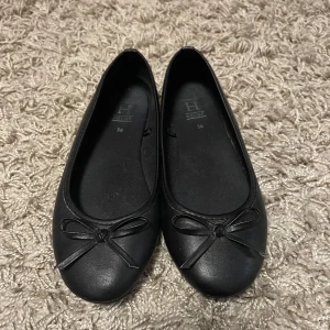 Svarta ballerinaskor med rosett från House - Svarta ballerinaskor från House med rund tå och dekorativ rosett framtill. Skorna har en klassisk och enkel design med platt sula, perfekta för en stilren look.