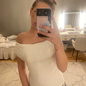 Vit offshoulder topp - Säljer en vit offshoulder topp med tight passform. Toppen har en bred, vikt kant över axlarna och är ärmlös. Perfekt för en stilren och enkel look.