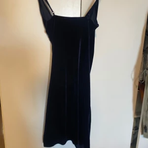 Mörkblå sammetsklänning med omlott - Säljer en elegant mörkblå sammetsklänning från NA-KD med omlottdesign och smala axelband. Klänningen har en figurnära passform och är perfekt för festliga tillfällen. Mjuk sammet ger en lyxig känsla och snygg lyster.