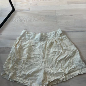 Krämvita shorts från Gina Tricot - Säljer ett par krämvita shorts från Gina Tricot med bred resår i midjan. De är luftiga och har en lös passform, perfekta för varma dagar. Materialet känns mjukt och bekvämt mot huden.