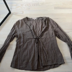 Brun blus med rosett vid bysten  - Brun blus med en v-ringad hals. 