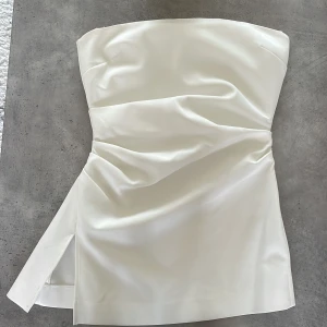 Vit bandeau topp från Zara - Säljer en stilren bandeau topp från Zara i storlek S. Den har en slits på sidan och dragkedja. Knappt använd och i mycket bra skick!