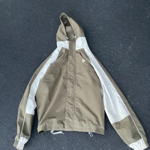 jacka från Harlaut med vitt & oliv färg - Snygg grön och vit vindjacka med huva från Harlaut. Jackan har dragkedja men den är ut bytt från den originella och har knappar framtill samt två stora fickor. Perfekt för blåsiga dagar och enkel att matcha med det mesta. Den har fått lite gråa märken på vänster arm från en rail men syns inte så mycket. Och de som man spänner med där nere har gått sönder men den funkar om man knyter. Modellen heter 2012