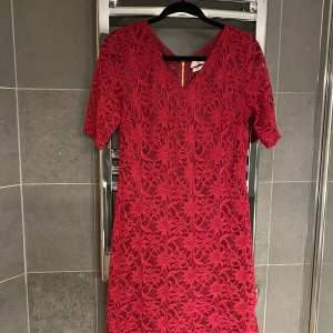 Röd spetsklänning från Angel - Säljer en röd spetsklänning från Angel med v-ringning och korta ärmar. Klänningen har dragkedja bak och är täckt av vacker spets. Perfekt för dig som vill sticka ut med en färgstark look. Knappt använd. Stl Large. 