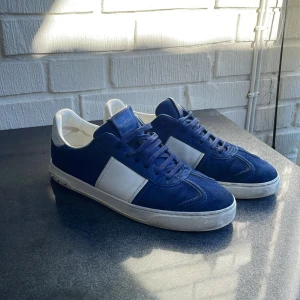 Valentino Flycrews - Snygga blå och vita sneakers från Valentino med coola nitar på hälen. Skorna har en klassisk snörning och är tillverkade i mocka och skinn. Perfekta för att ge din outfit en stilfull touch.