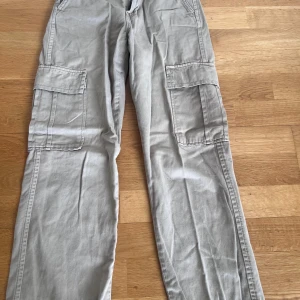 Beiga cargopants från STAR - Säljer ett par beiga cargopants från STAR med stora fickor på sidorna och klassisk cargomodell. Byxorna har normal passform och stängs med dragkedja och knapp. Perfekta för en avslappnad stil.