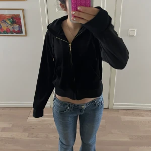 Svart velourjacka från Juicy Couture - Säljer en svart velourjacka från Juicy Couture med dragkedja och huva. Jackan har en broderad logga på bröstet och guldfärgade detaljer. Perfekt för en avslappnad och stilren look. är väldigt liten i storleken så sitter som en S