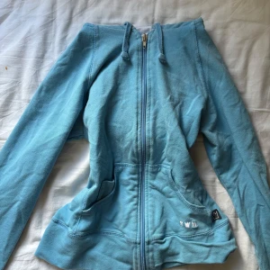 Ljusblå tränings zip up - figurnära passform, har blekta fläckar men syns knappt.