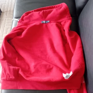 Röd hoodie från Polo Ralph Lauren - Säljer en röd hoodie från Polo Ralph Lauren med dragkedja och huva. Tröjan har två fickor framtill, vit dragsko och den klassiska broderade loggan på bröstet. Perfekt för en avslappnad stil.