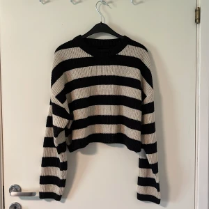Svart och beige randig stickad croppad tröja - Säljer en stickad tröja med breda svarta och beige ränder. Tröjan är croppad och har lång ärm samt rund halsringning. Perfekt för dig som gillar en avslappnad och trendig stil. Nypris 369kr. 