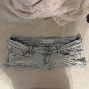 Ljusblå slitna jeansshorts Tally Weijl - Ljusblå jeansshorts från Tally Weijl med låg midja och slitna detaljer framtill och baktill. Klassisk femficksmodell med dubbla knappar och dragkedja. Perfekta för en chill sommarlook.