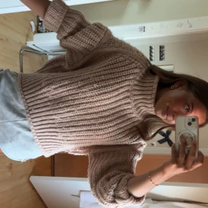 Beige stickad tröja med ribbad struktur - Mysig beige stickad tröja med grov ribbad struktur och hög hals. Tröjan har lång ärm och en loose fit som ger en avslappnad vibe. Perfekt för lager-på-lager och passar till både jeans och mjukisbyxor.