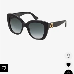 Svarta cat-eye solglasögon från Gucci - Snygga svarta solglasögon från Gucci med cat-eye form och breda skalmar. Glasen är tonade i grått och på sidorna finns den ikoniska guldiga GG-loggan. Ramen är i blank plast som ger en lyxig känsla och passar perfekt för dig som vill sticka ut.