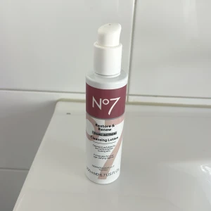 No7 Restore & Renew Cleansing Lotion - No7 Restore & Renew Dual Action Cleansing Lotion i en vit och vinröd pumpflaska, 200 ml. Rengör och exfolierar huden för en fräsch och klar känsla. Perfekt för att förbereda huden inför sminkrutinen.