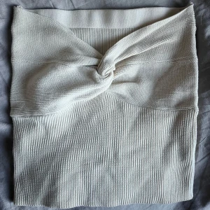 Vit stickad bandeu top med twistdetalj - Supersnygg vit stickad bandeu top med twistad knut framtill. Kjolen är ribbstickad och har en tight passform som framhäver siluetten. Perfekt att styla med en croppad topp eller oversized hoodie för en trendig look. Aldrig använd 