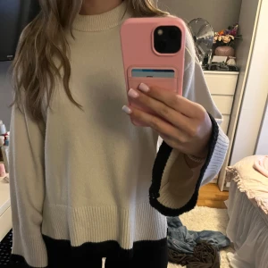 Beige stickad tröja från Gina Tricot - Säljer en beige stickad tröja från Gina Tricot med svarta detaljer längst ner på ärmar och nederkant. Tröjan har en rak, loose passform och ribbade muddar. Perfekt för dig som gillar en enkel men snygg stil.