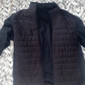 Svart quiltad dunjacka från Zara - Svart dunjacka från Zara i storlek L med quiltad framsida och hög krage. Jackan har en stilren look med diskreta sömmar och dragkedja framtill. Perfekt att slänga över en hoodie eller tröja för extra värme. Materialet är syntet och polyester.