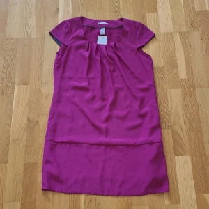 Cerise kortklänning från H&M - Snygg cerise kortklänning från H&M. Blusmaterial. Helt ny, prislappen kvar. Nypris 199 kr. 