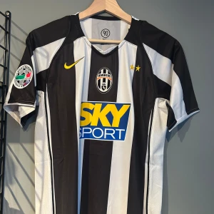 Juventus Ibrahimović 9 matchtröja Nike - Juventus fotbollströja med klassiska svarta och vita ränder, officiellt Serie A-märke på ärmen och tryck med Ibrahimović 9 på ryggen. Nike-logga i gult, två stjärnor på bröstet och SKY SPORT sponsortryck. Svalt funktionsmaterial, kortärmad modell. En replika helt ny med tagg!