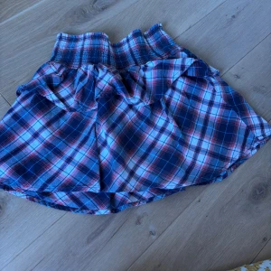 Rutig kortkjol från Petrol Industries - Supersöt rutig kortkjol från Petrol Industries i blått, vitt och rött. Kjolen har bred smock i midjan och volangdetaljer upptill för en extra cool look. Perfekt för dig som gillar en avslappnad men trendig stil.